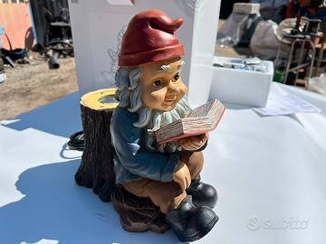 Gnomo seduto su un tronco mentre legge un libro