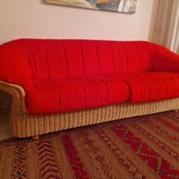 Divano da interno in midollino, con cuscini rossi.