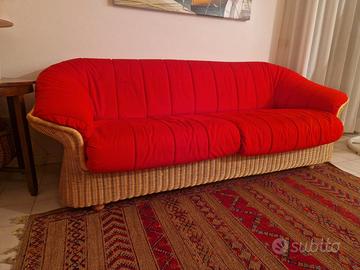 Divano da interno in midollino, con cuscini rossi.