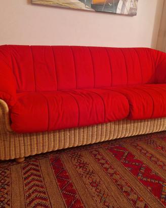 Divano da interno in midollino, con cuscini rossi.