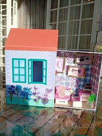 Scatola casa con mobili e gattino addormentato.