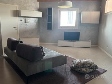 Sala con divano, tappeto, cuscini, tv, lampada