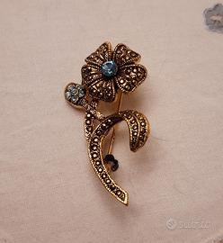 Spilla dorata con brillantini azzurri.